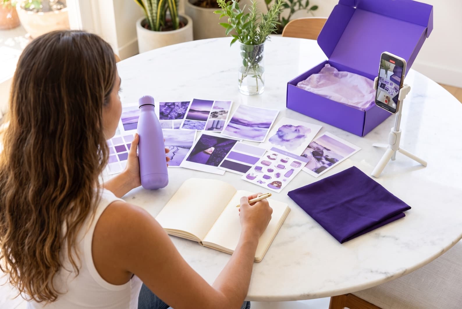 Creator planejando um novo capítulo com produto, referências visuais, cartela e celular sobre a mesa
